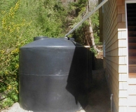 Rain water catchment tank farm. 'Dry' connecting pipe from gutter to tank. Filter basket inside tank access lid. San Juan Is. WA.
